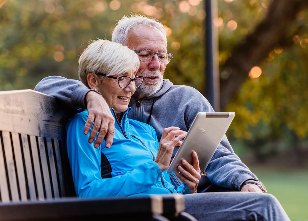 Couple using a tablet on a bench outside